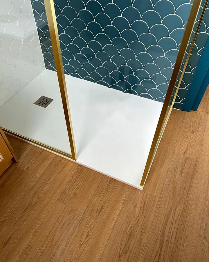 Douche vitrée à profilés dorés avec un carrelage bleu et un sol à effet bois.
