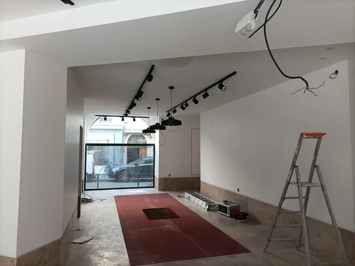 Local commercial en travaux avec des rails de spots et un escabeau.