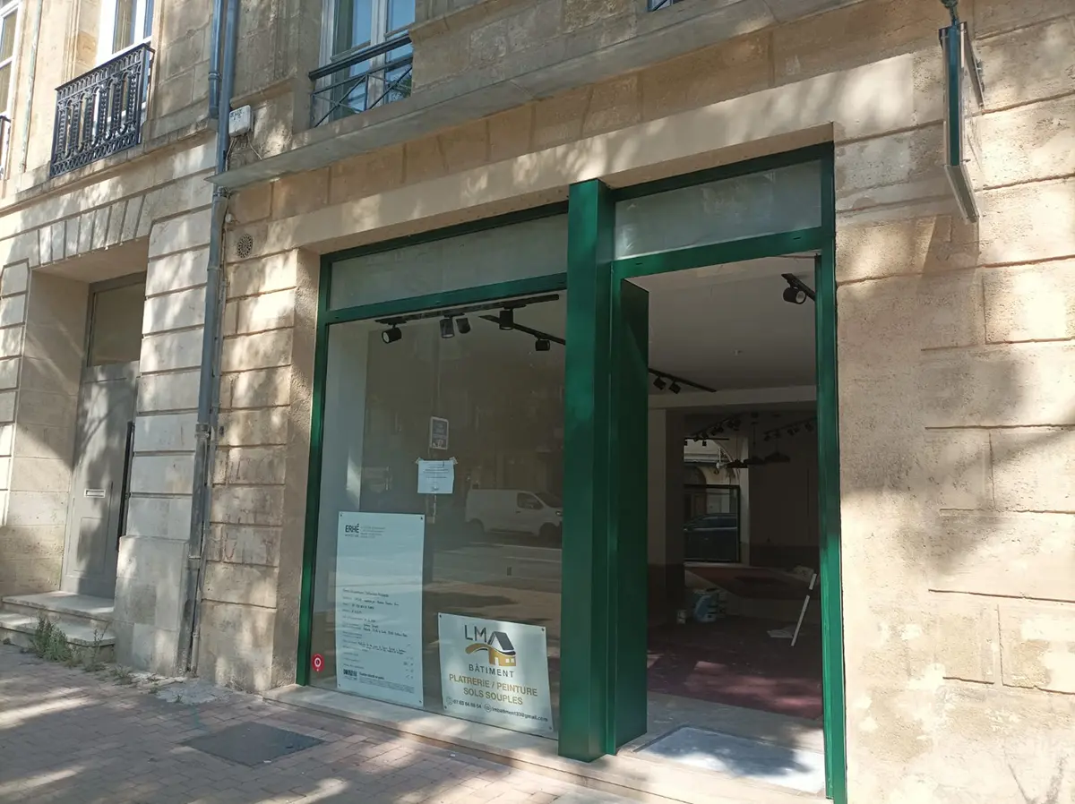 Devanture verte d’un commerce dans un immeuble en pierre.