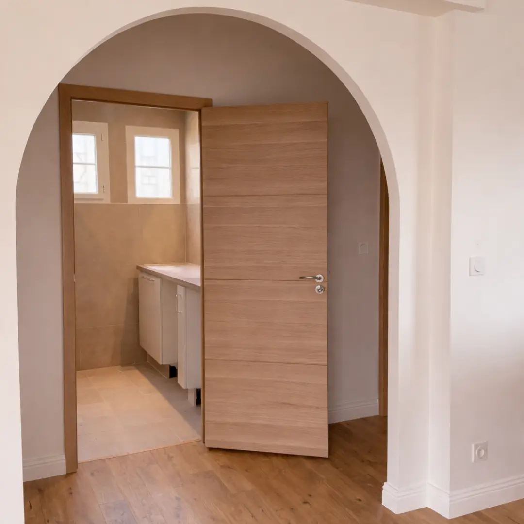 Ouverture cintrée blanche donnant sur une porte en bois et une pièce carrelée.