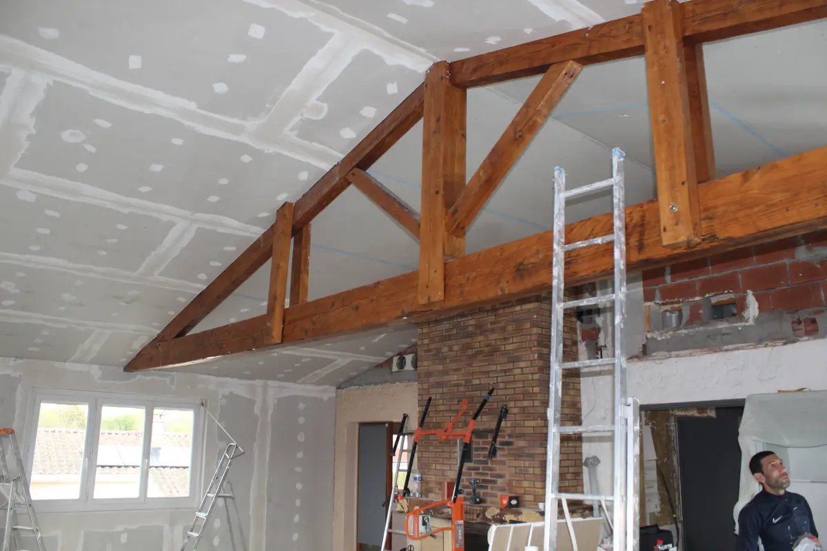Plafond en plaques de plâtre autour d’une charpente en bois apparente.