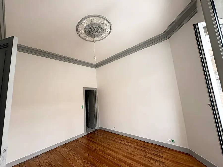 Pièce avec une rosace, des corniches grises et un plancher en bois.