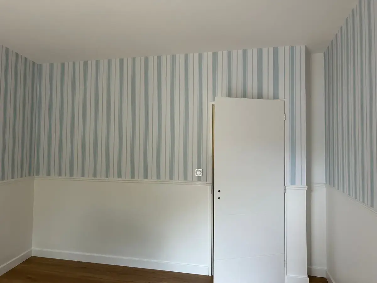 Mur à papier peint rayé au-dessus d’un soubassement blanc.
