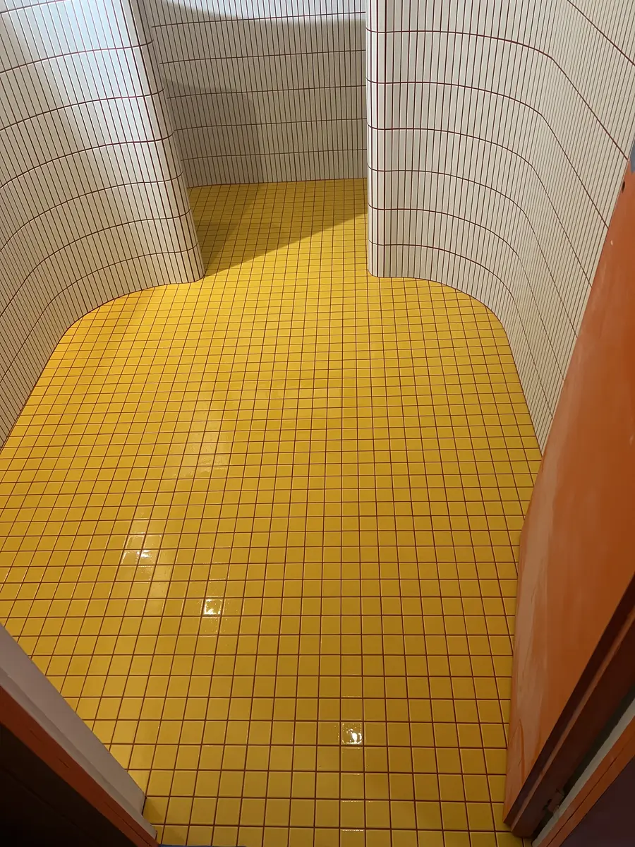 Espace de douche aux parois arrondies, avec un sol carrelé jaune.